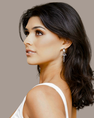 Model Woman wearing a white top with CVLCHA ADIRA Rod Hoop Earrings featuring a sculptural hoop design with polished rod detail and signature chain drop.