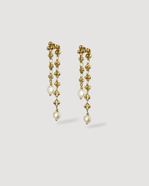 close up of CVLCHA_Alina pearl drop dangling gold earrings with a light grey back gorund 