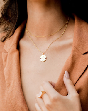 Close-up of a women wearing a CVLCHA Cancer Gold necklace with a zodiac pendant, set against a neutral background.