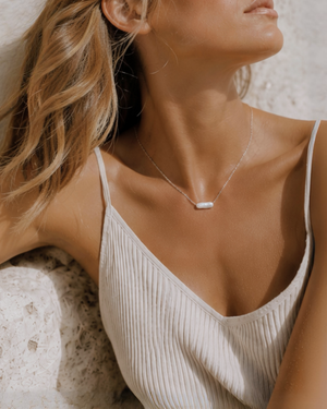 Woman wearing a delicate pearl necklace necklace, modern everyday pearl necklace, sitting, relaxing in the sun on a stone surface.