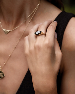 Close-up of a hand wearing a  striking modern cvlcha gold black Marquise statement cocktail  ring with a blurred background.