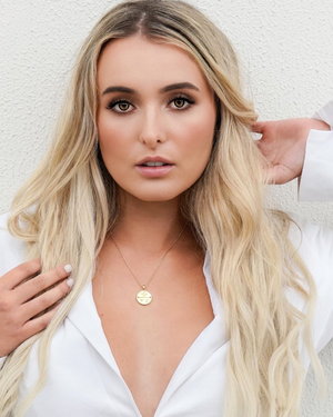 Woman with long blonde hair wearing a gold necklace against a white background