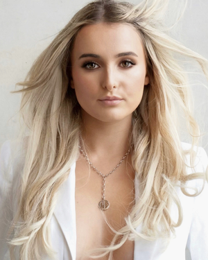 Woman with long blonde hair wearing =a CVLCHA Origin Y-Drop Silver necklace in a white top and necklace against a light background