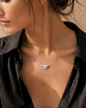 Close-up of a woman wearing cvlcha evil eye protect your peace silver necklace  against a neutral background.